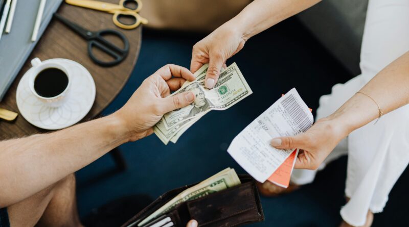 Close-up of a transaction with US dollar bills and receipts being exchanged over a table with coffee and scissors.