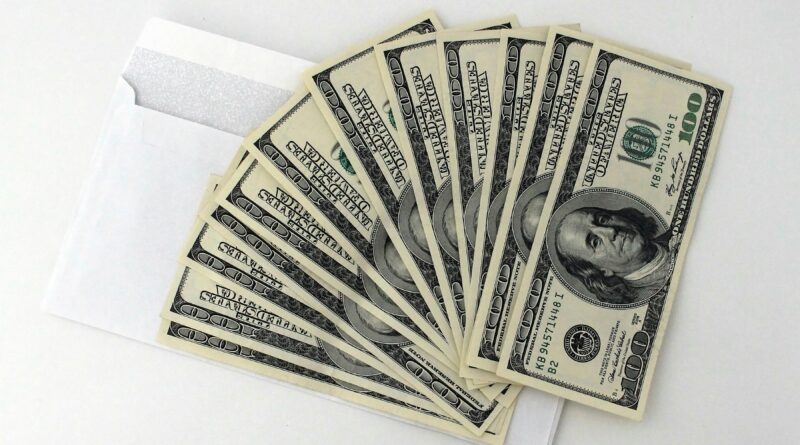 Fan of US $100 bills partially out of a white envelope on a white background.