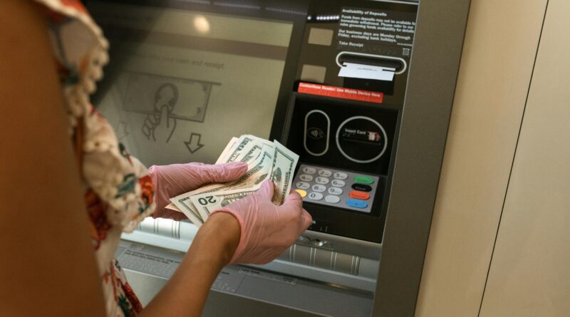 A person wearing gloves withdraws cash from an ATM, ensuring hygiene.