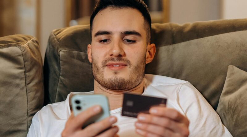 Young man using smartphone and credit card for online shopping indoors.