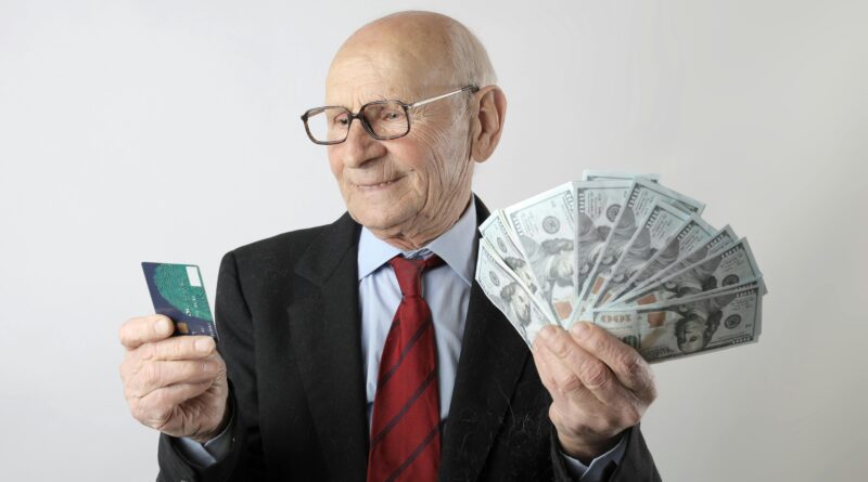 Elderly man in a suit holding a credit card and US dollar bills, representing finance and wealth.