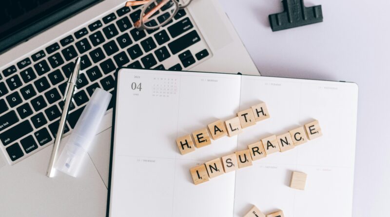 Scrabble tiles spelling health insurance on a planner next to a laptop.